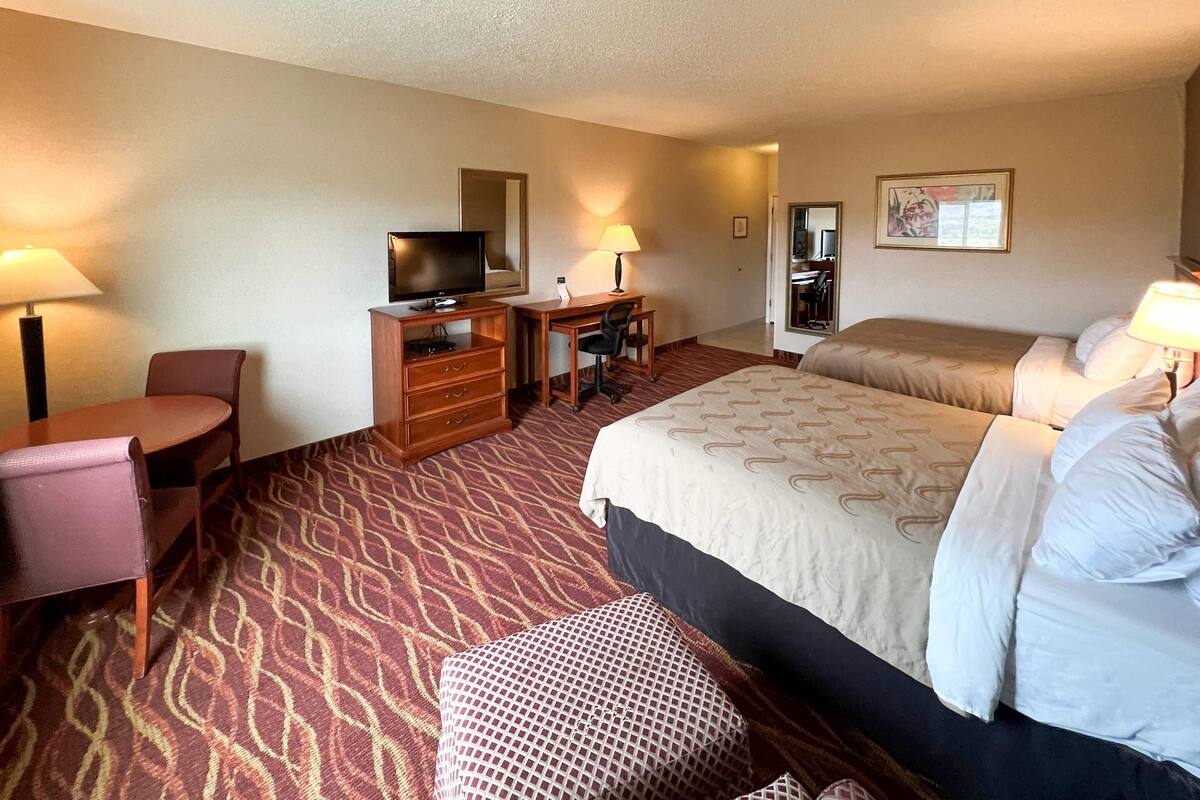 A hotel room with a bed, a desk with a chair, a television, and a small table.