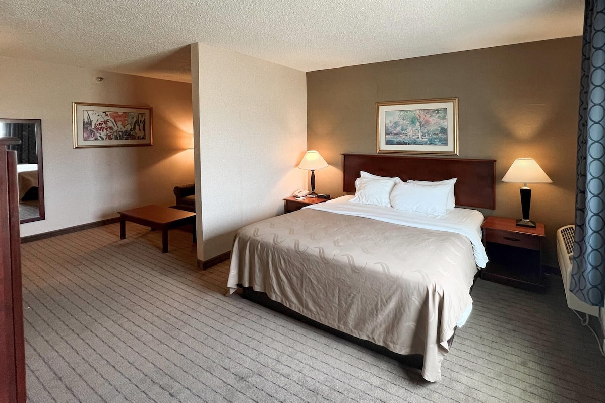 A hotel room with a large bed, two bedside tables, a desk, a chair, and two lamps.