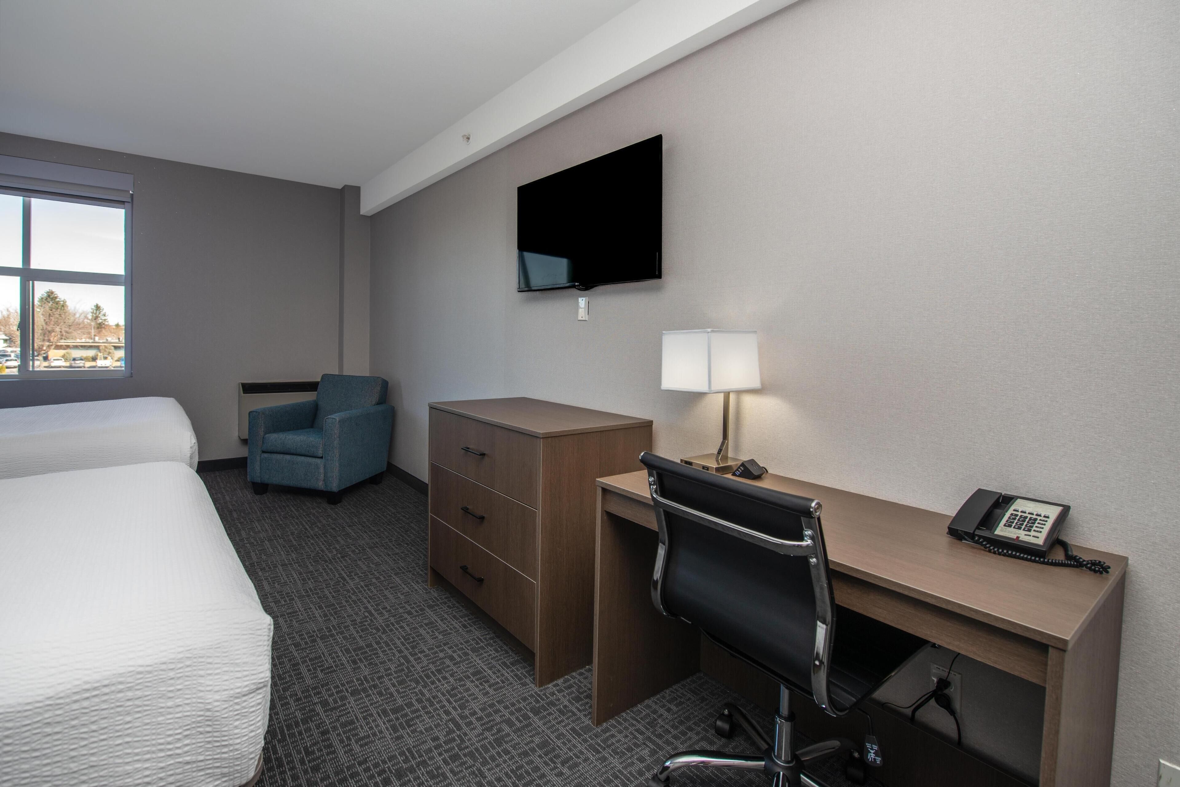 A hotel room with a bed, a desk with a chair, a dresser, a TV, and a lamp.