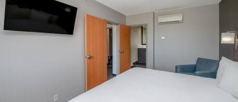 A hotel room with a bed, a television, a door, and an air conditioning unit.