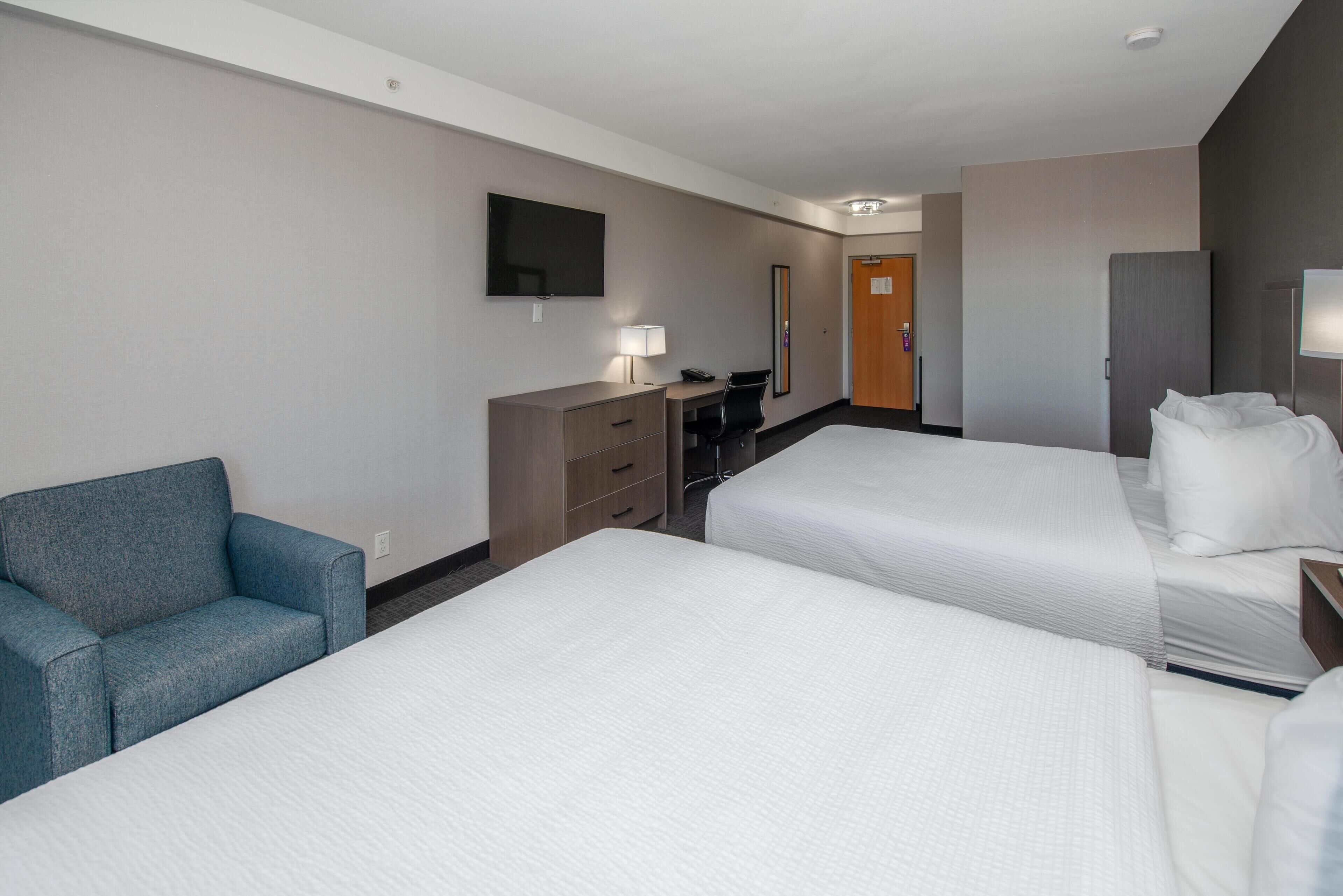 A hotel room with two beds, a desk, a chair, a TV, and a wardrobe.