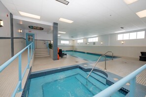 An indoor swimming pool with a tiled edge, a blue railing, and a staircase leading to an exit. - Coast Lethbridge Hotel & Conference Centre (Lethbridge)