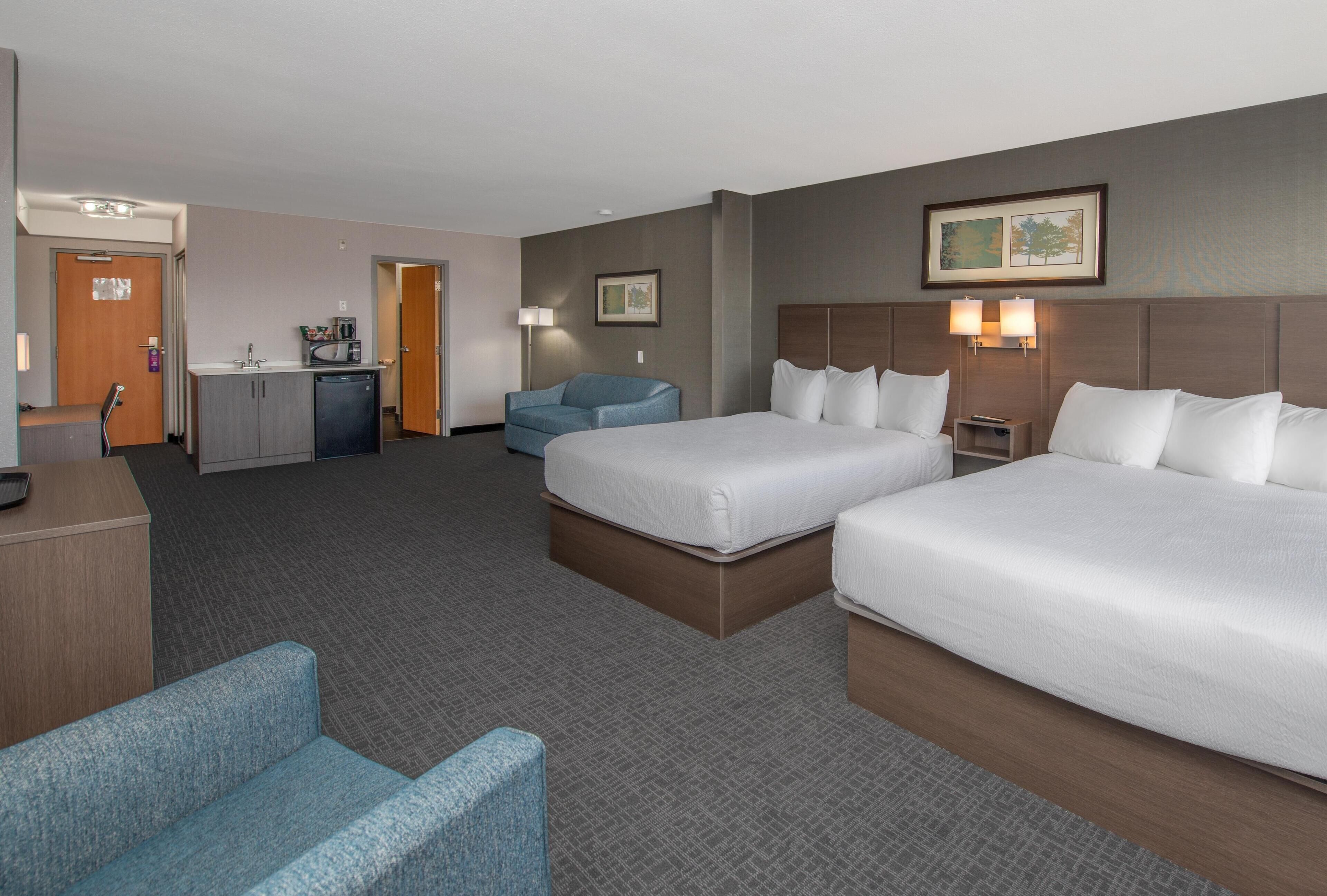 A hotel room with two beds, a desk, a chair, a microwave, and a small kitchenette.