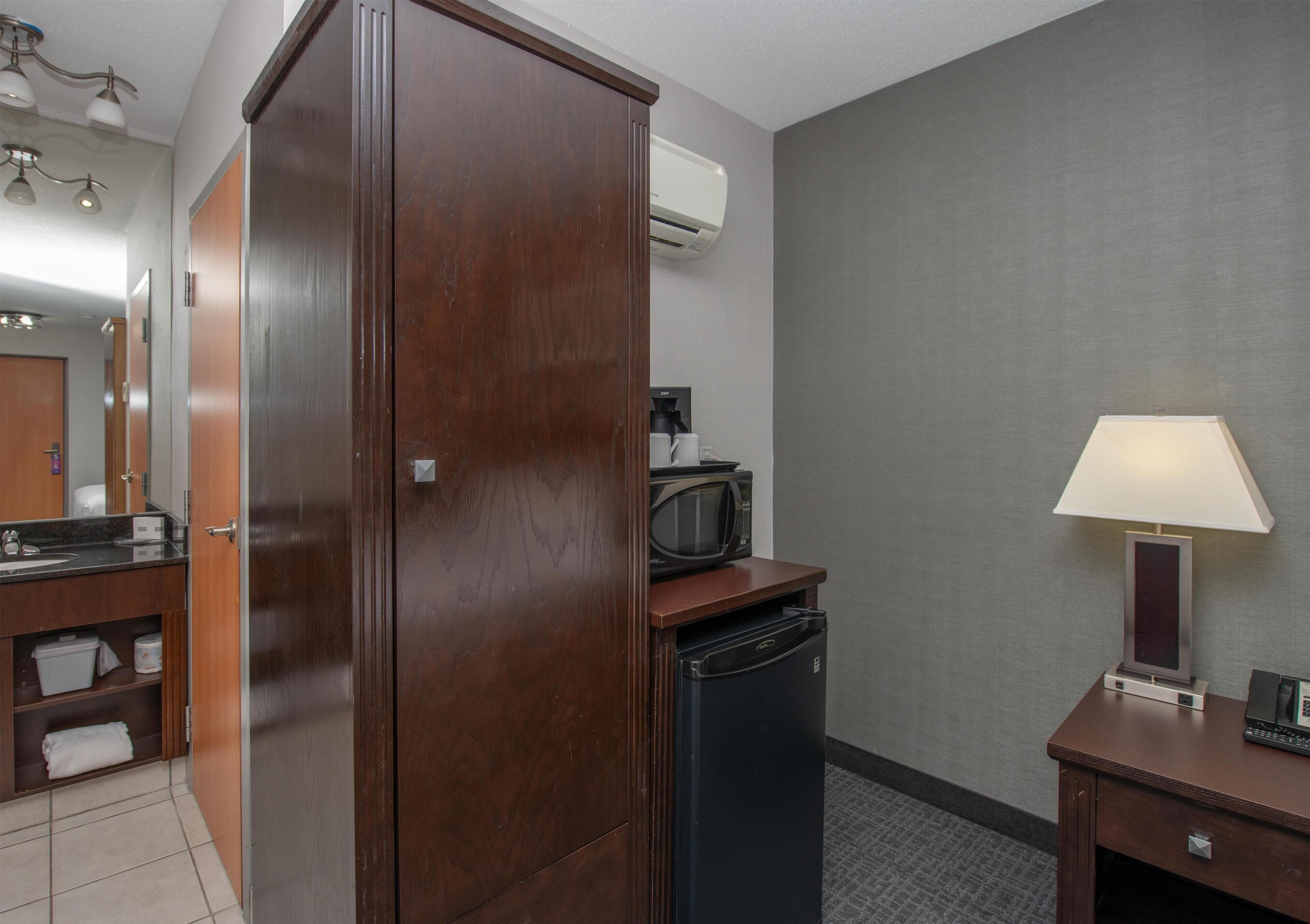 Une chambre d’hôtel équipée d’une armoire en bois, d’un four à micro-ondes, d’un réfrigérateur, d’un bureau avec une lampe et d’une petite table avec un téléphone.