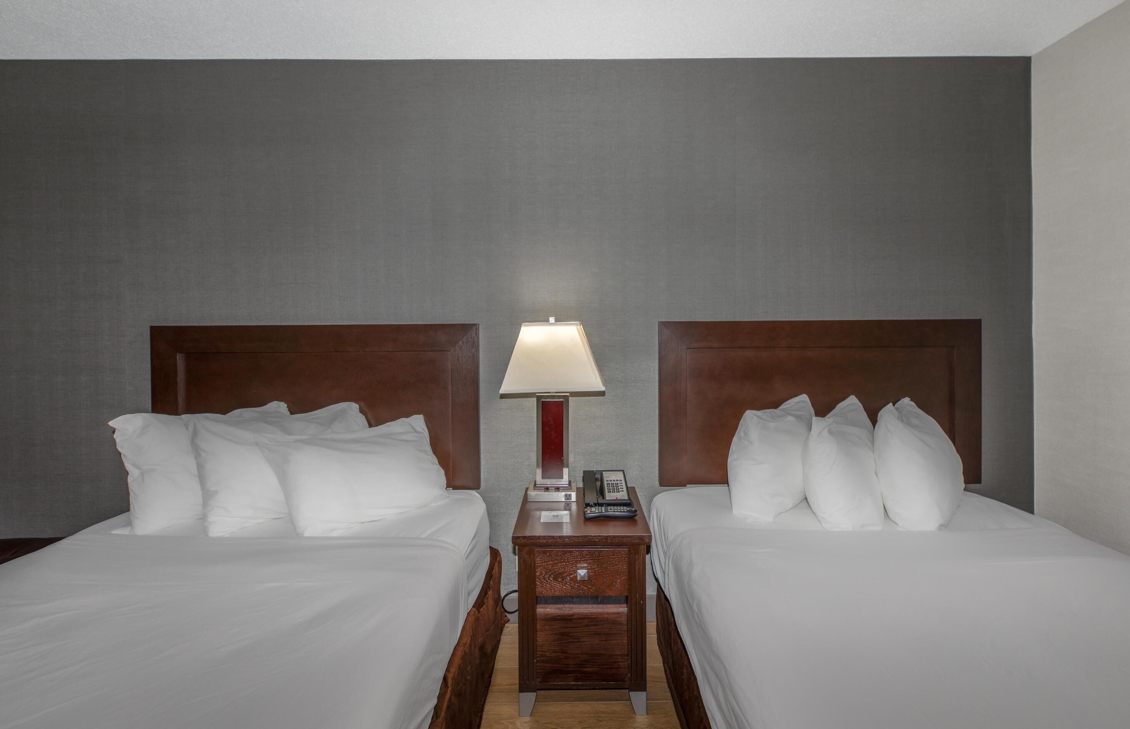 A hotel room with two beds, a nightstand with a lamp, and a telephone.
