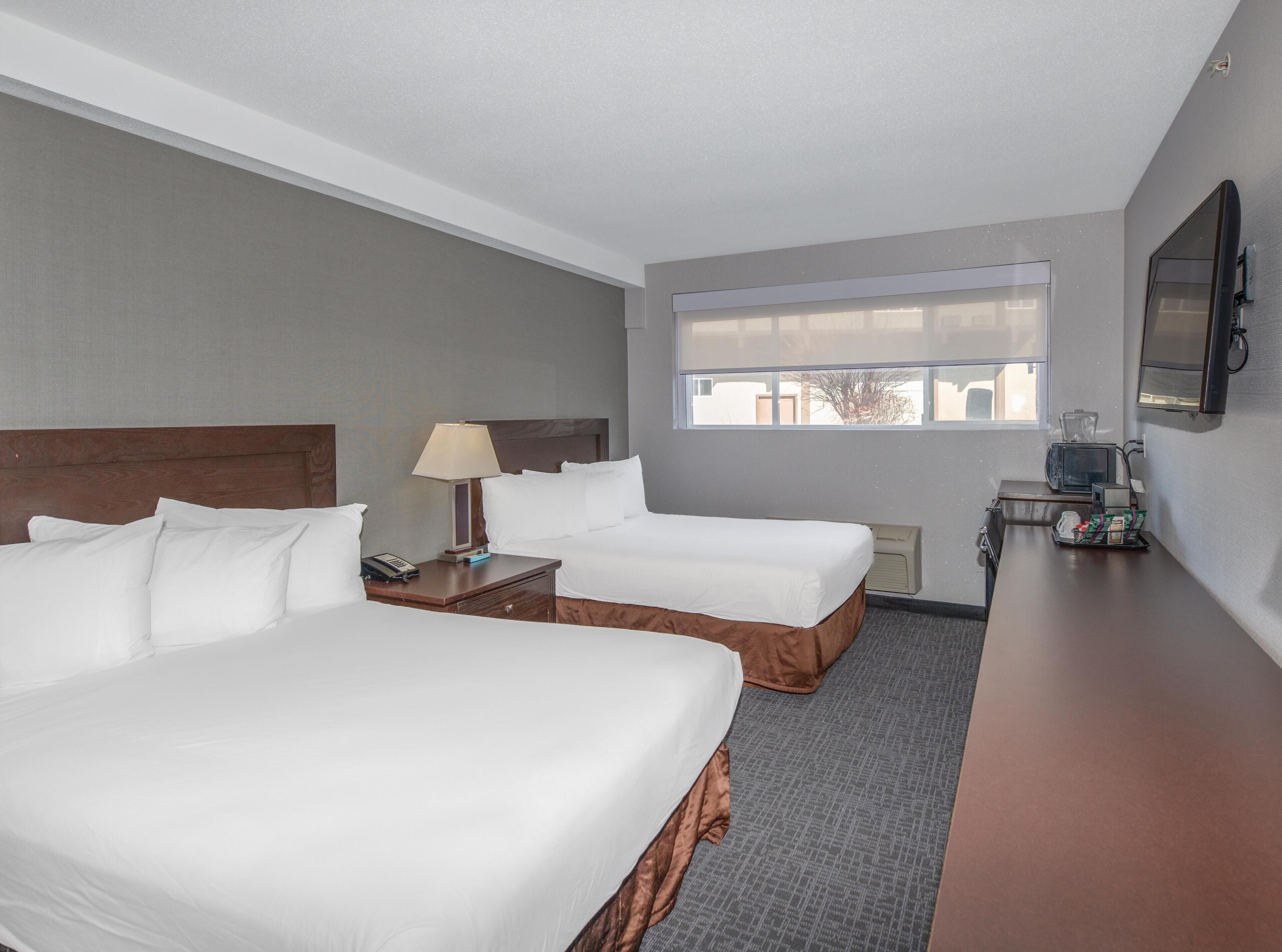 A hotel room with two beds, a desk, a lamp, a television, and a window.