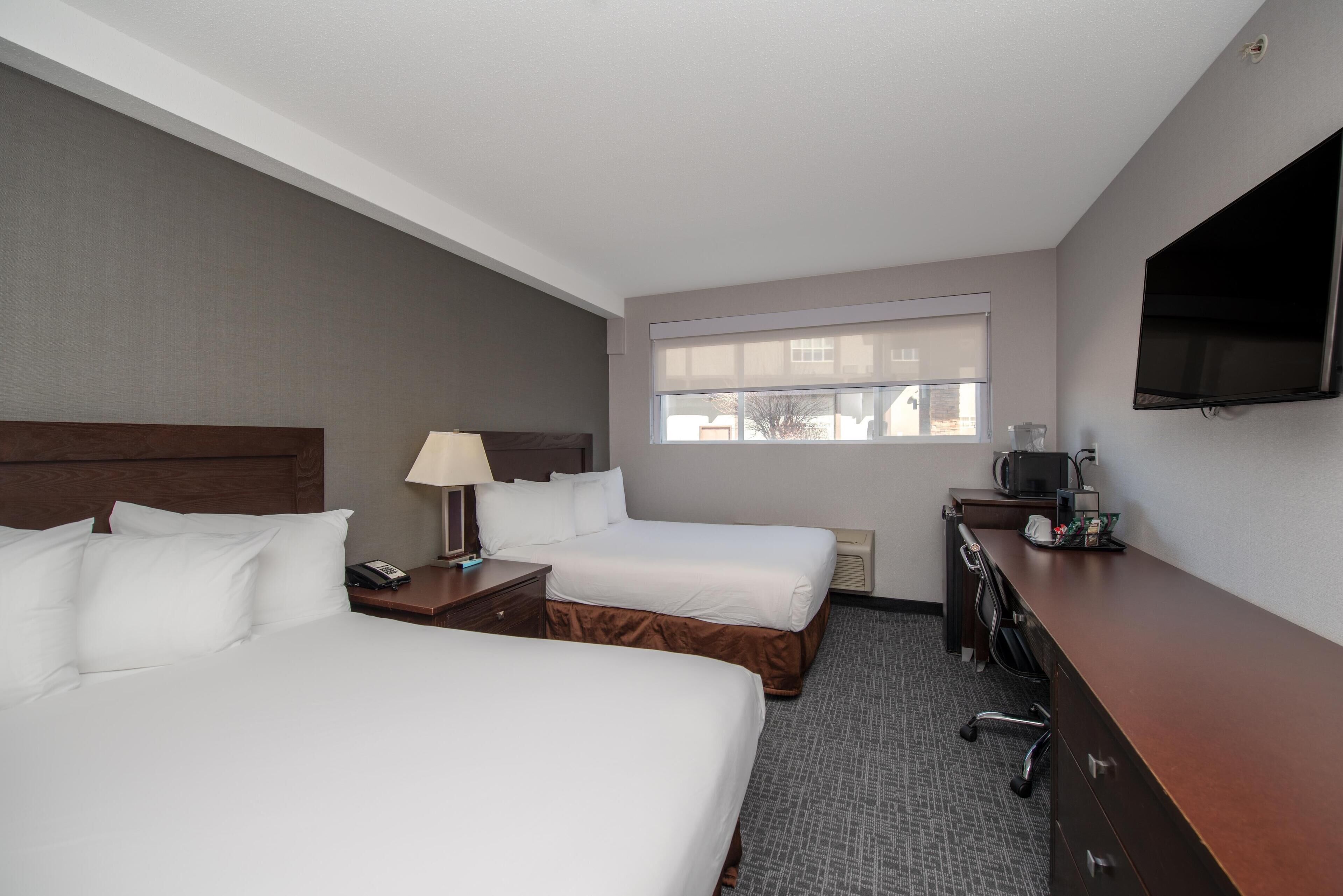 Quarto de hotel com duas camas, uma escrivaninha, uma televisão e uma janela.
