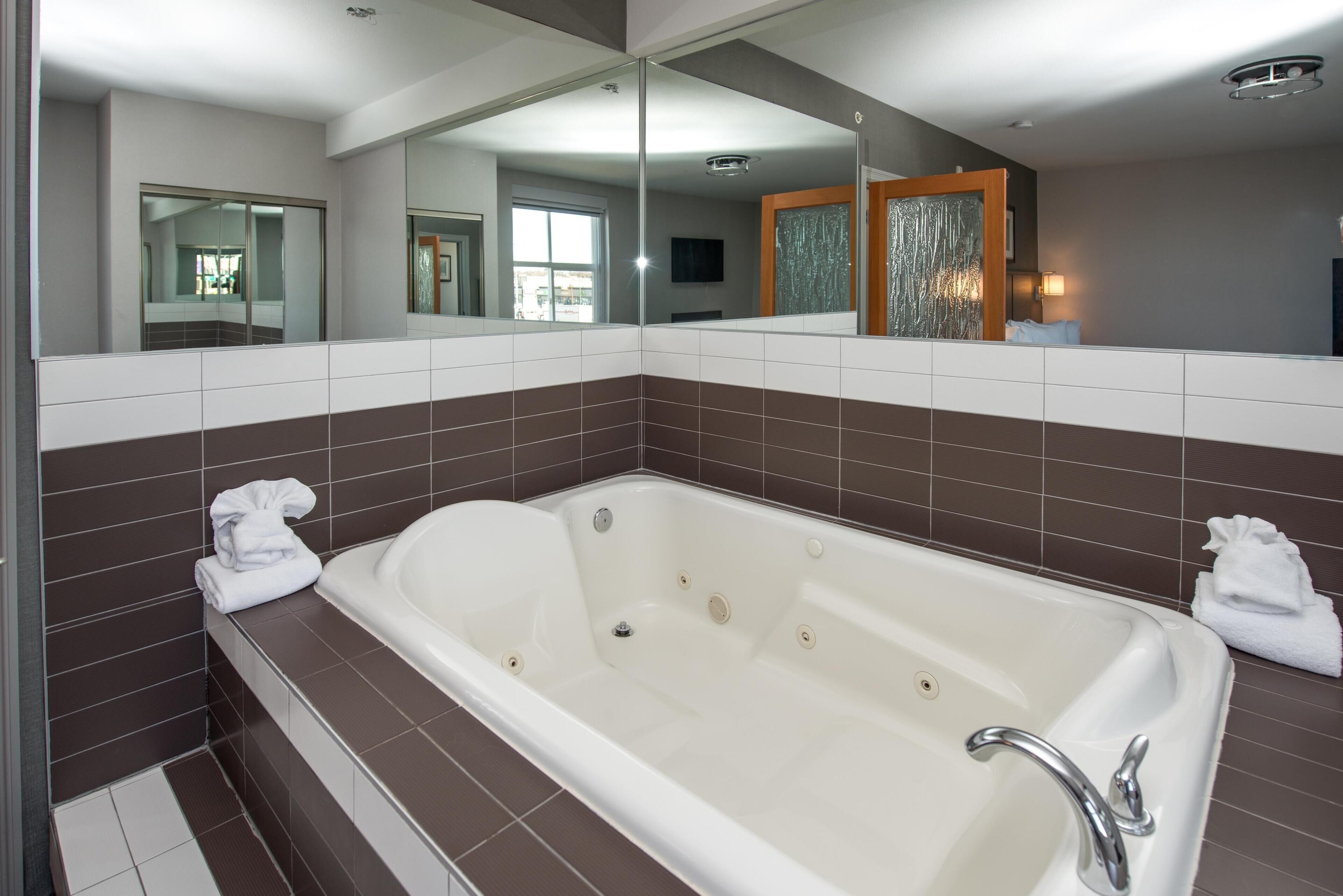 Un baño moderno con una bañera grande, un espejo y piso de baldosas.