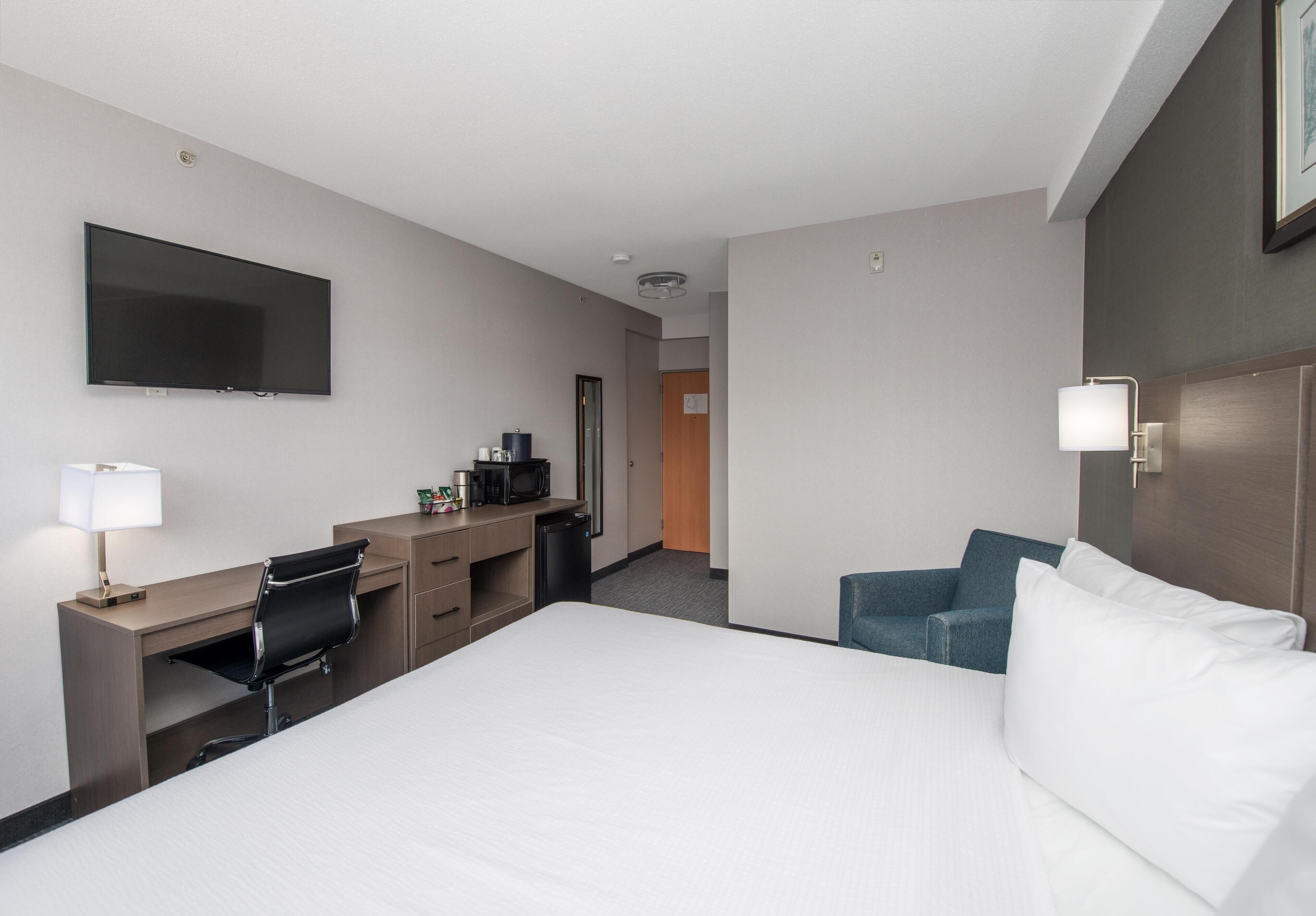 A hotel room with a bed, desk, chair, TV, and a door leading to a bathroom.