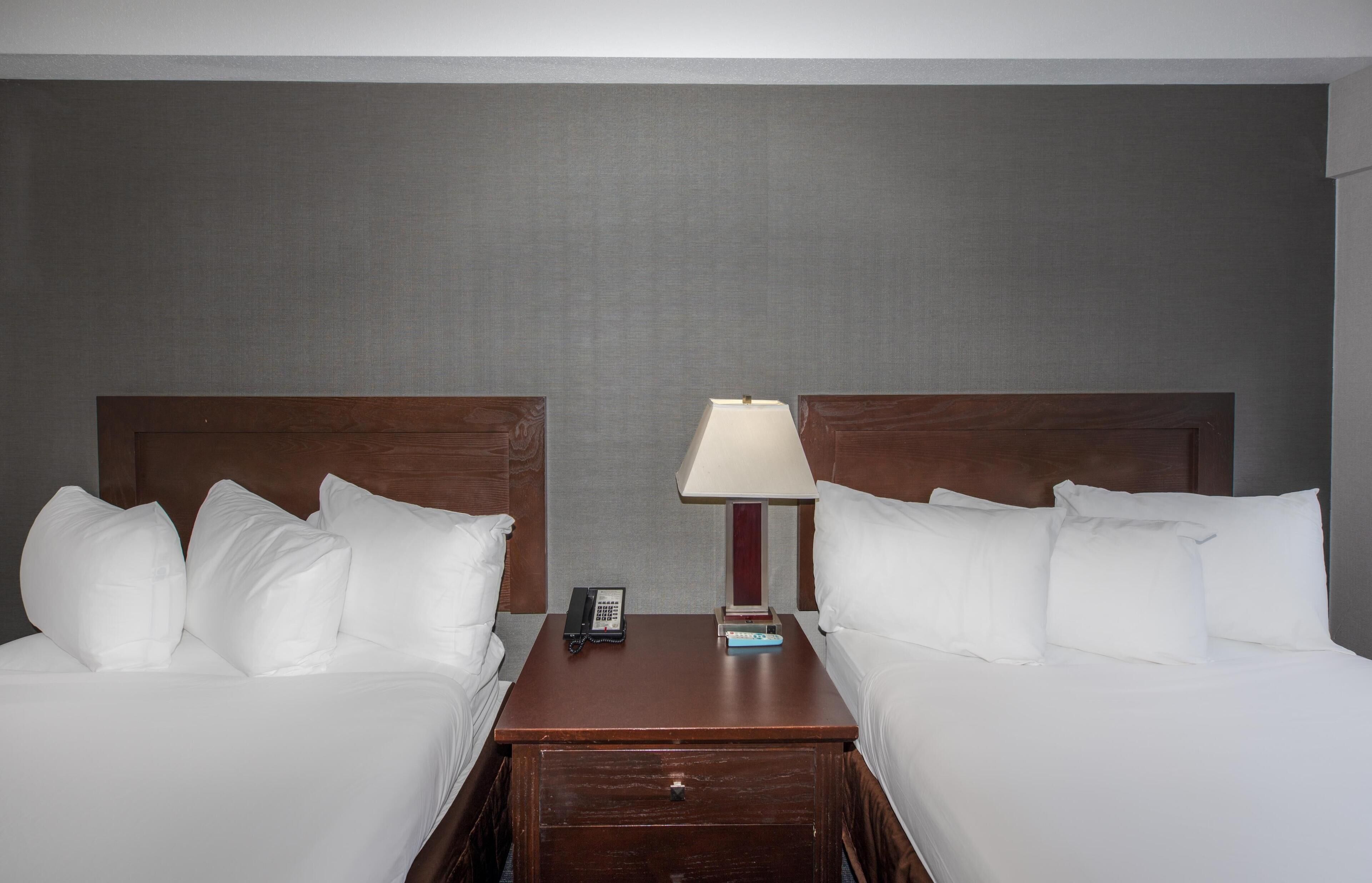 A hotel room with two beds, a nightstand with a lamp, and a phone.