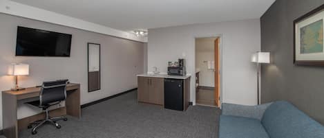 Ein Hotelzimmer mit Schreibtisch, Stuhl, Küchenzeile und einem blauen Sofa.