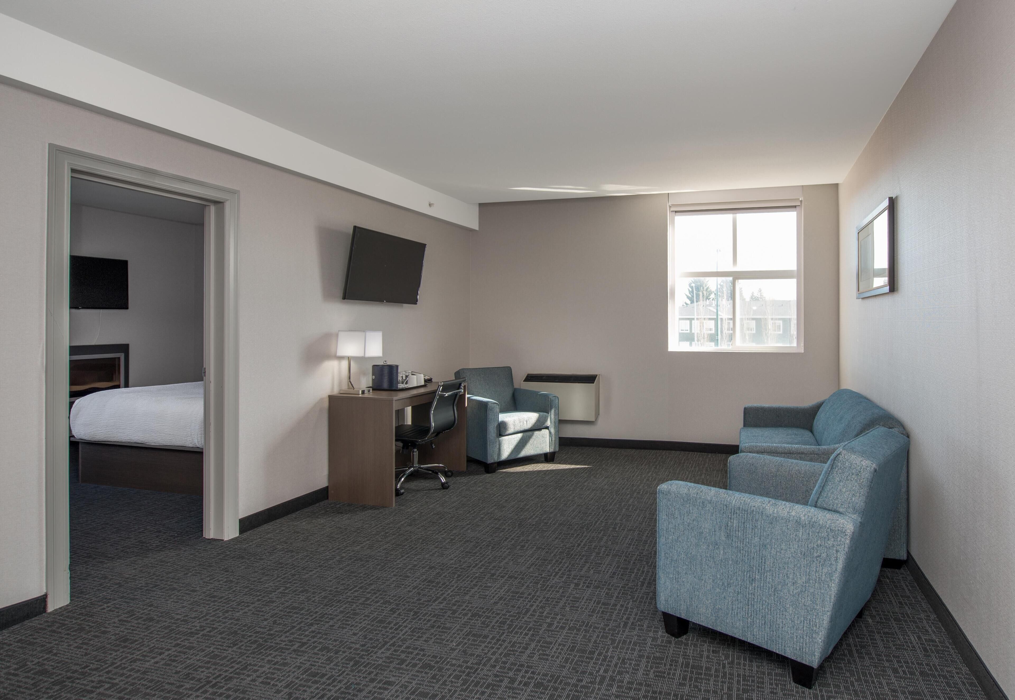 A hotel room with a bed, desk, two armchairs, a TV, and a window.