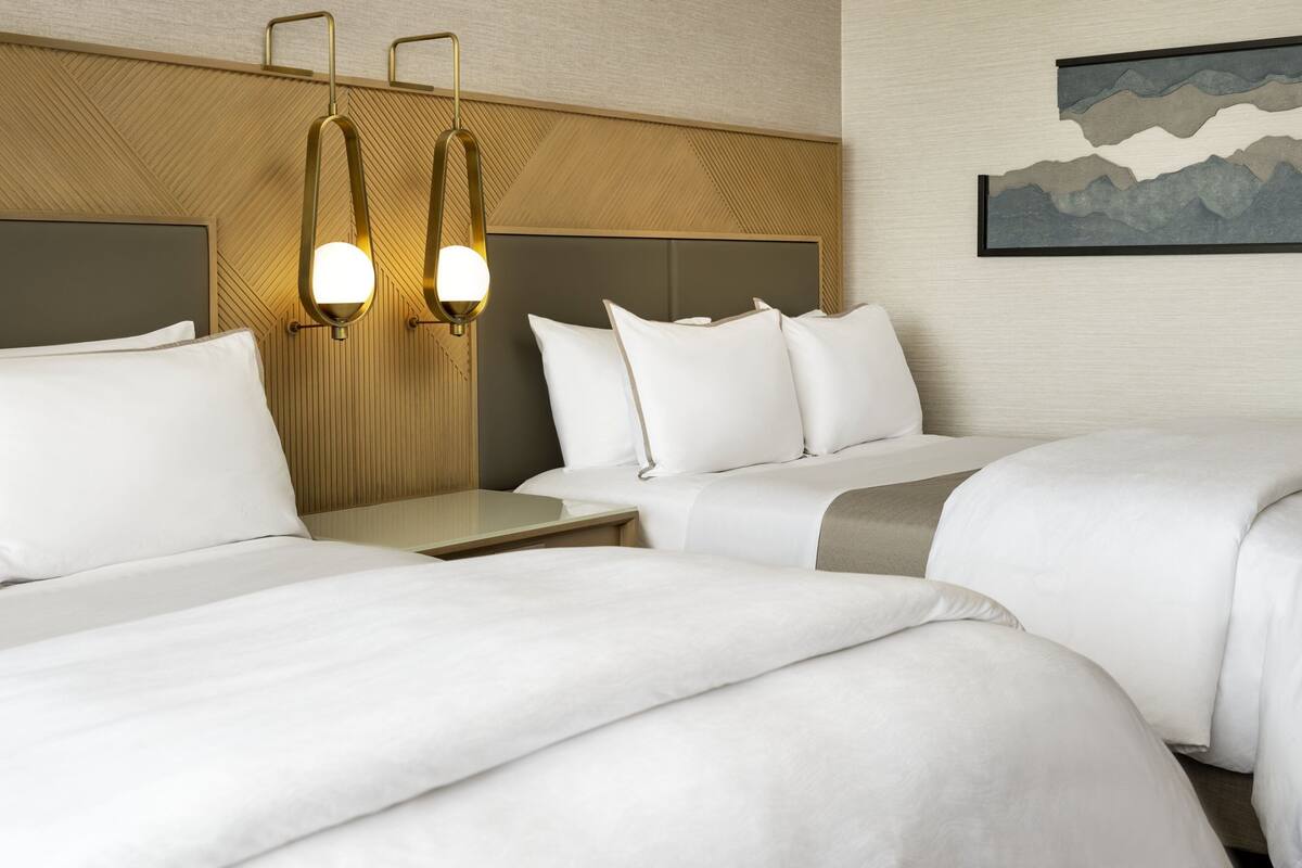 A hotel room with two beds, a nightstand, and wall-mounted lamps.