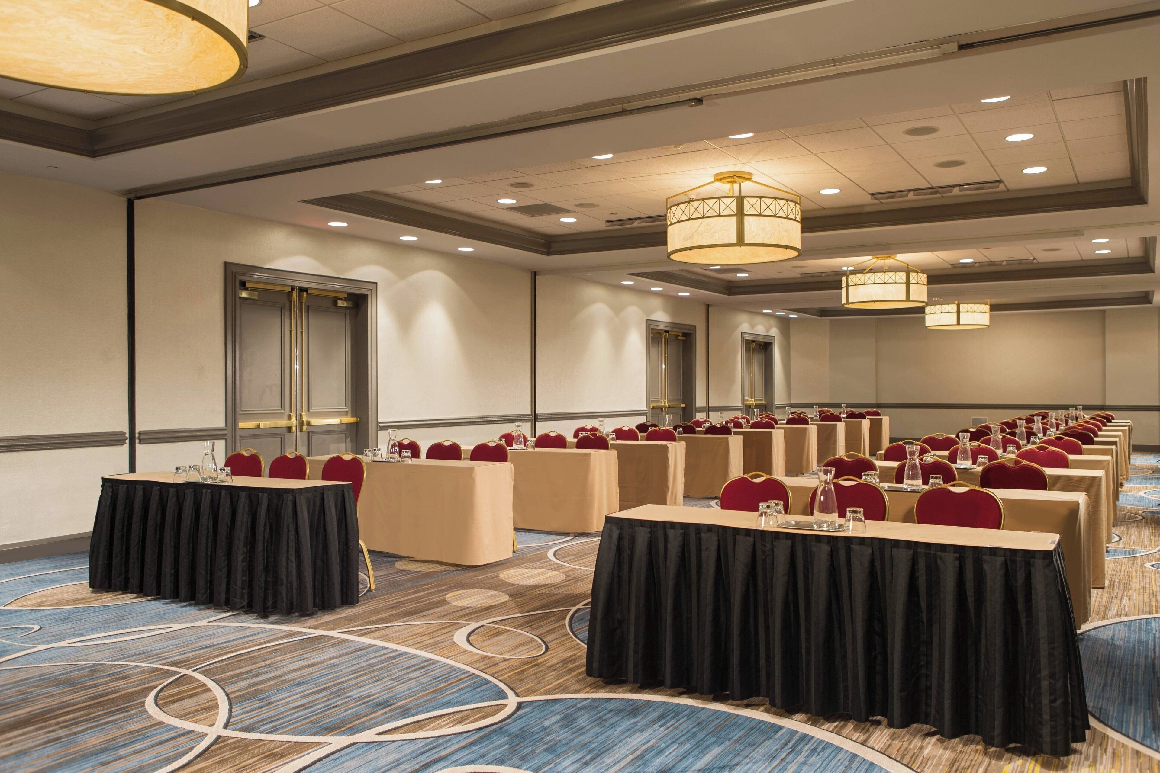 A conference room with rows of tables and chairs, equipped with nameplates and water bottles, in a modern hotel setting.