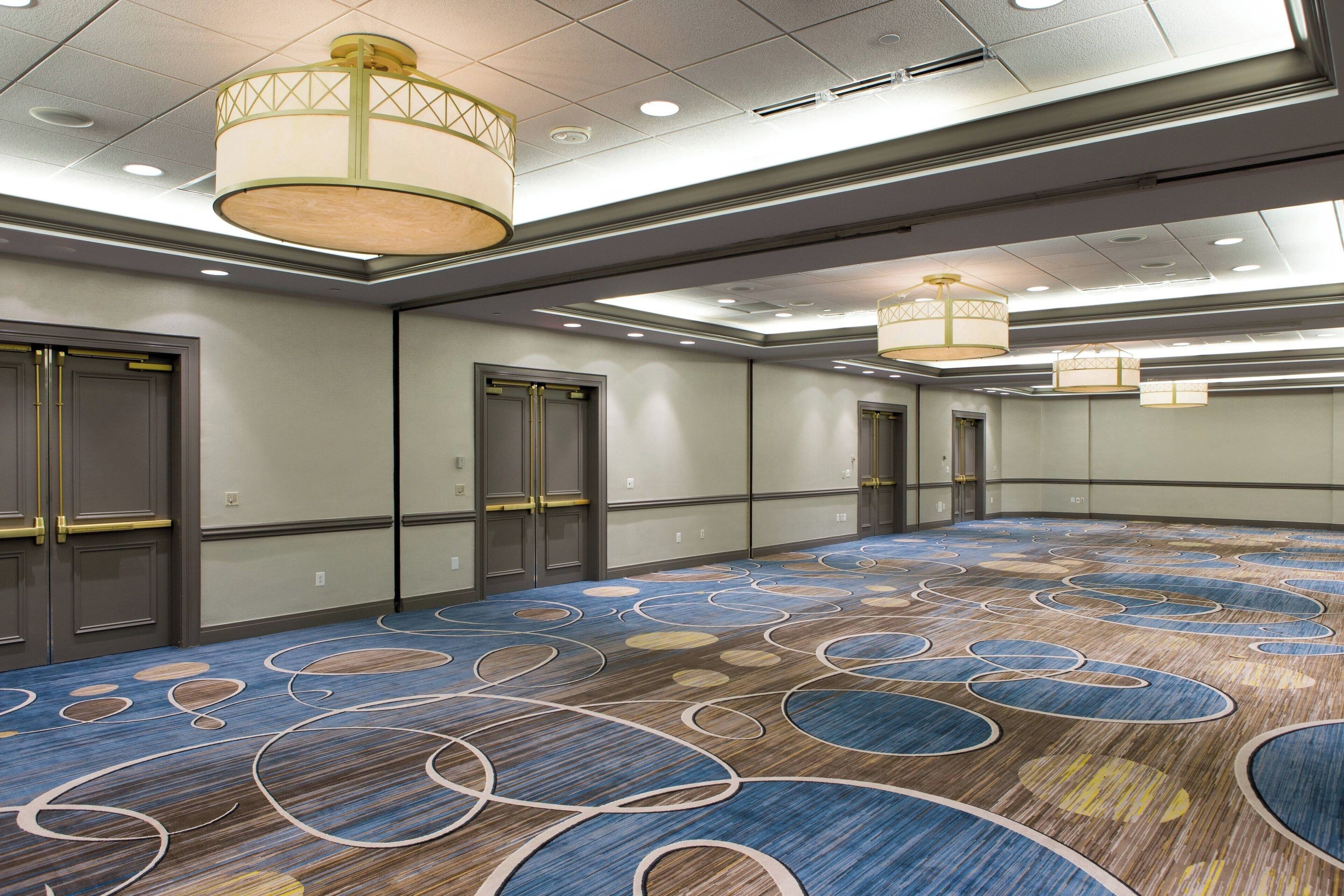 A large conference room with a patterned carpet, recessed lighting, and modern chandeliers.