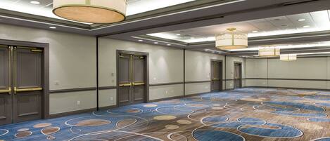 A large conference room with a patterned carpet, recessed lighting, and modern chandeliers.