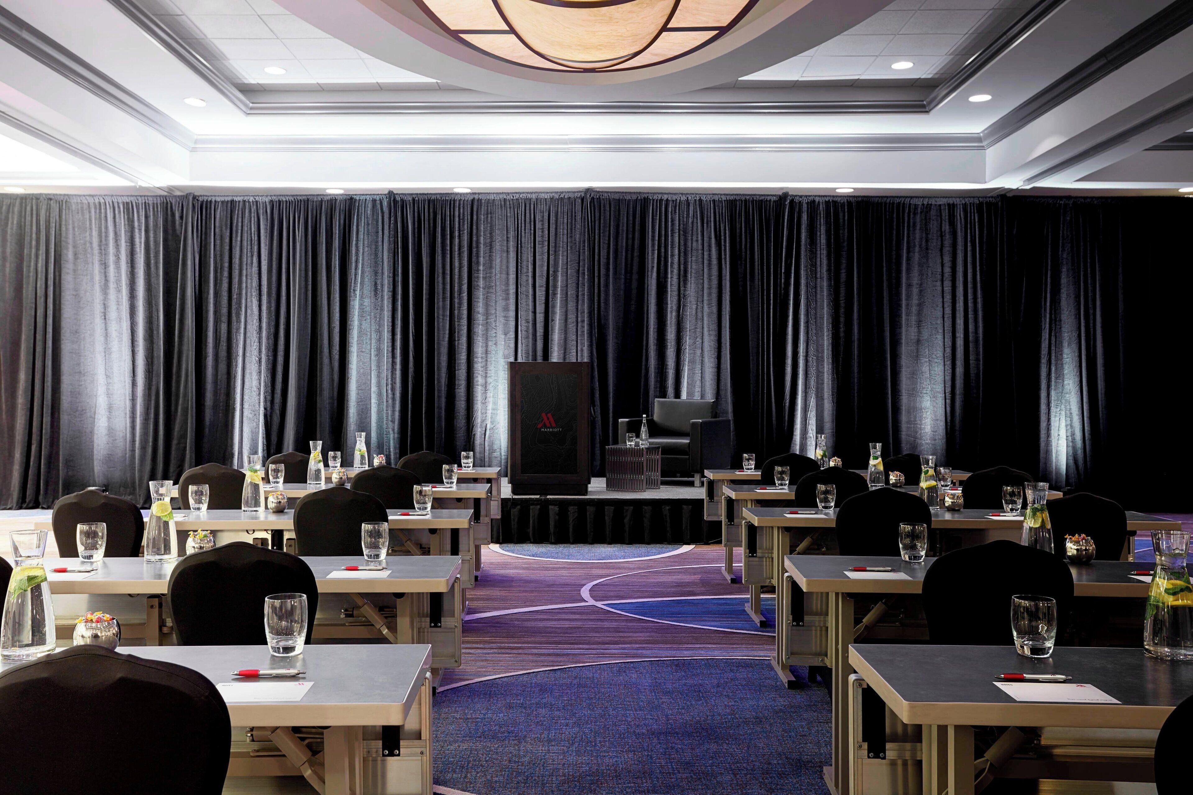 A conference room with tables, chairs, and a stage with a screen.