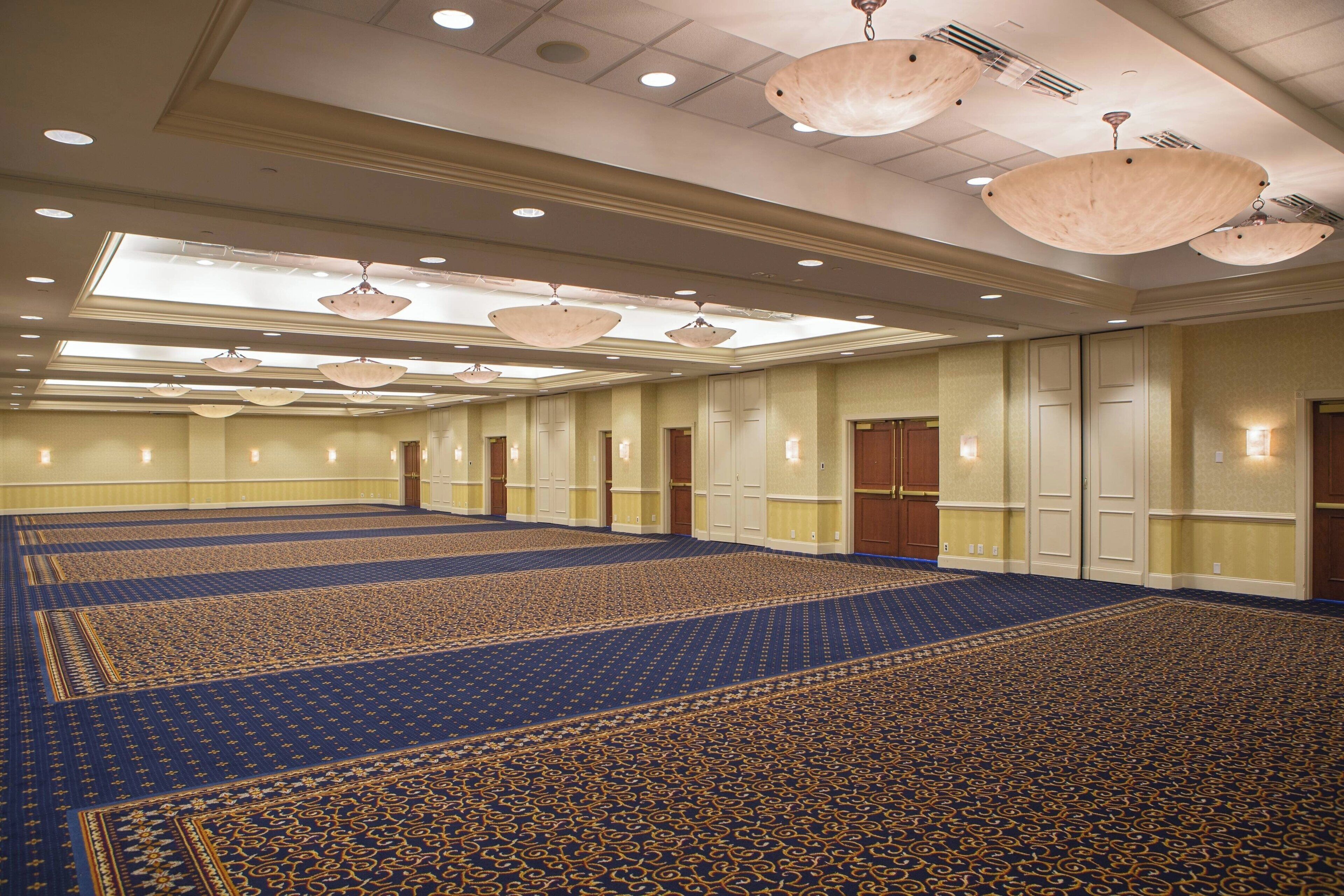 A large, well-lit conference room with a patterned carpet, multiple doors, and hanging chandeliers.