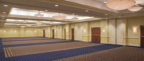 A large, well-lit conference room with a patterned carpet, multiple doors, and hanging chandeliers.