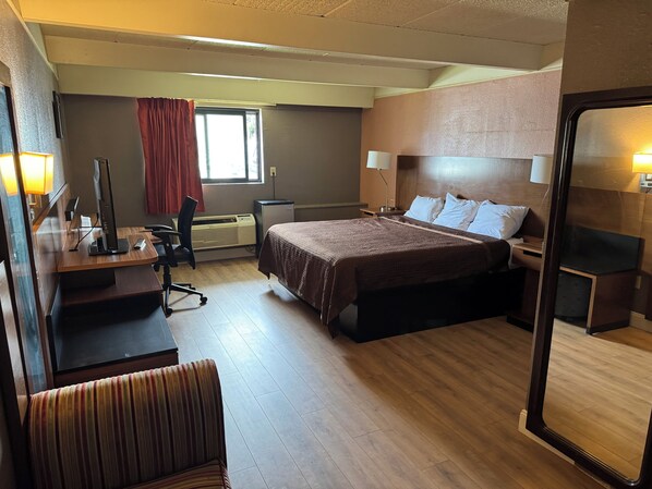 A hotel room with a bed, desk, chair, and a large mirror.