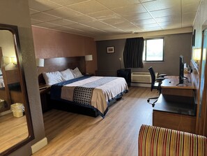 A hotel room with a bed, desk, chair, and a window.