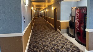 A hotel hallway with a patterned carpet, wall-mounted lights, a Coca-Cola vending machine, and a door at the end. - Economy Inn North Randall (North Randall)