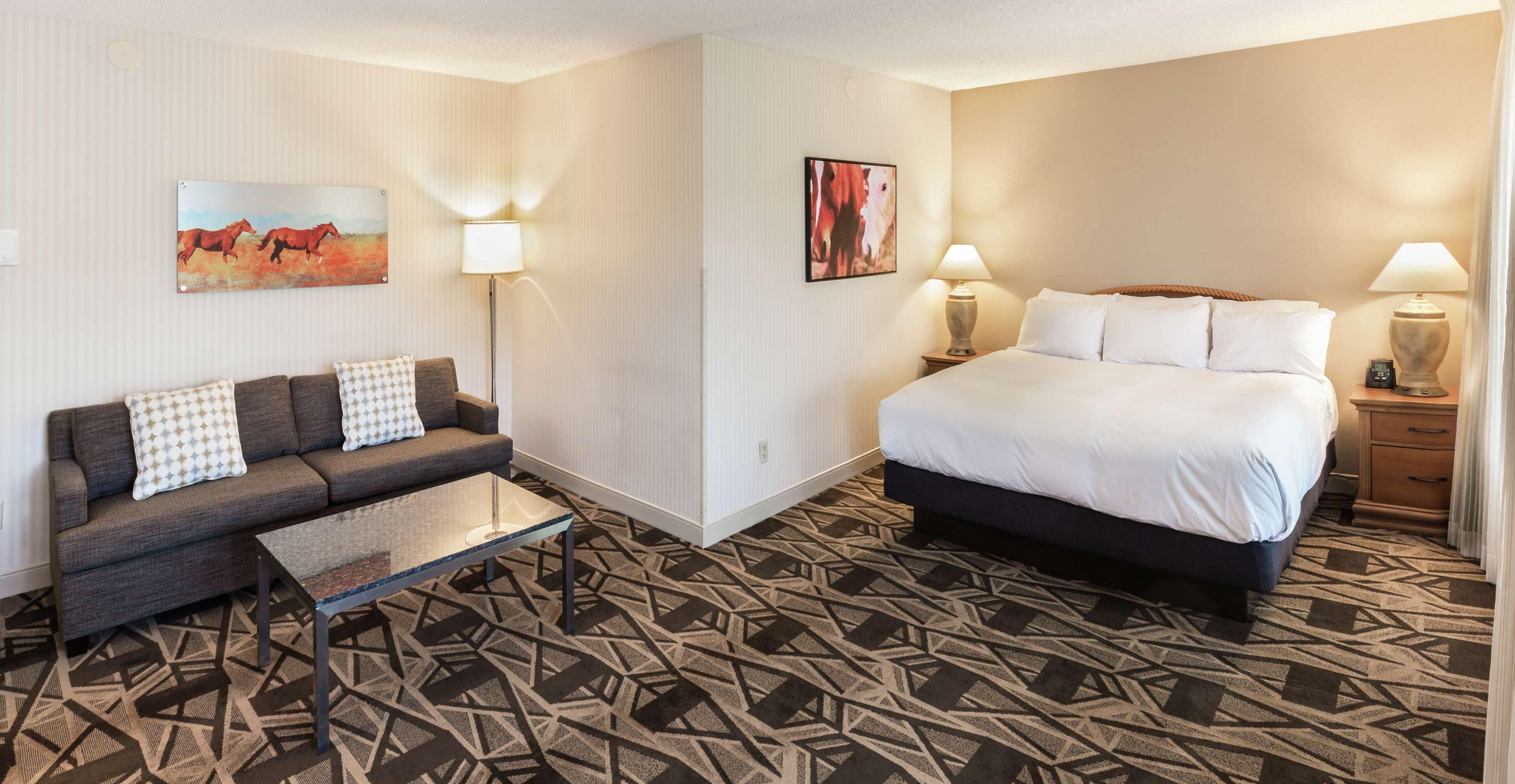 Habitación de hotel con cama, sofá, mesa de centro y dos lámparas de pared.