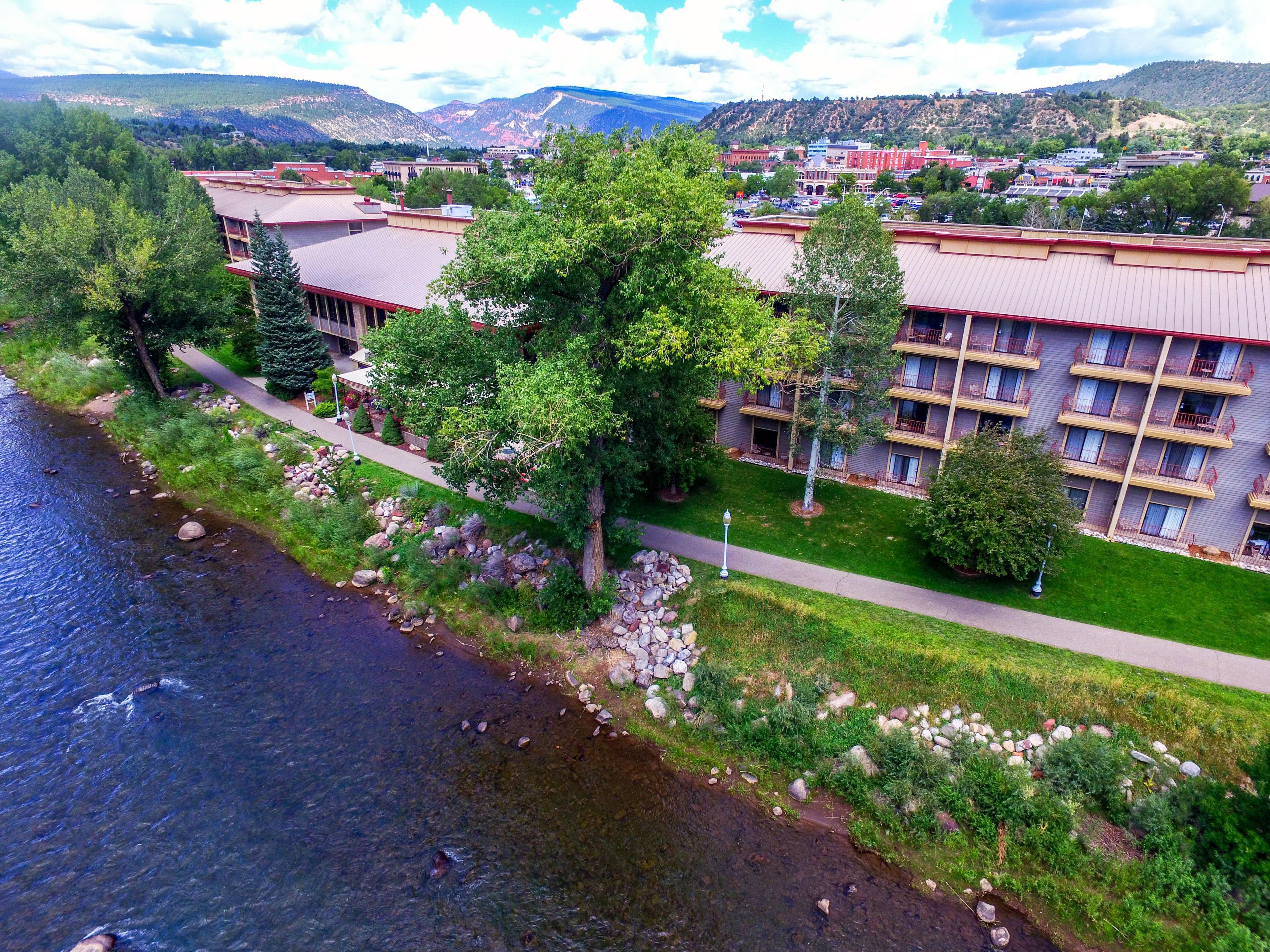 Een hotel met meerdere verdiepingen, een rivier op de voorgrond en een bergachtig achtergrond.