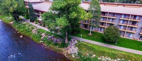 Een hotel met meerdere verdiepingen, een rivier op de voorgrond en een bergachtig achtergrond.