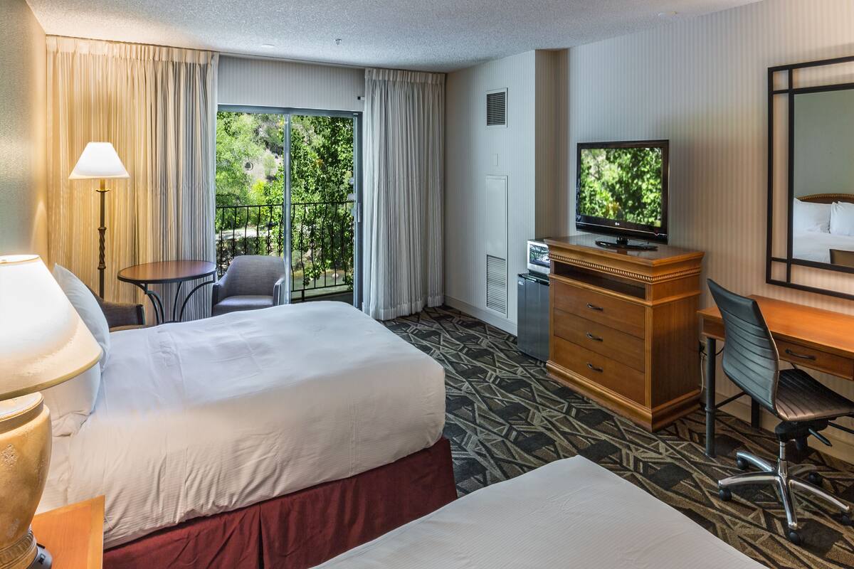 A hotel room with a bed, a desk, a chair, a television, and a window with curtains.