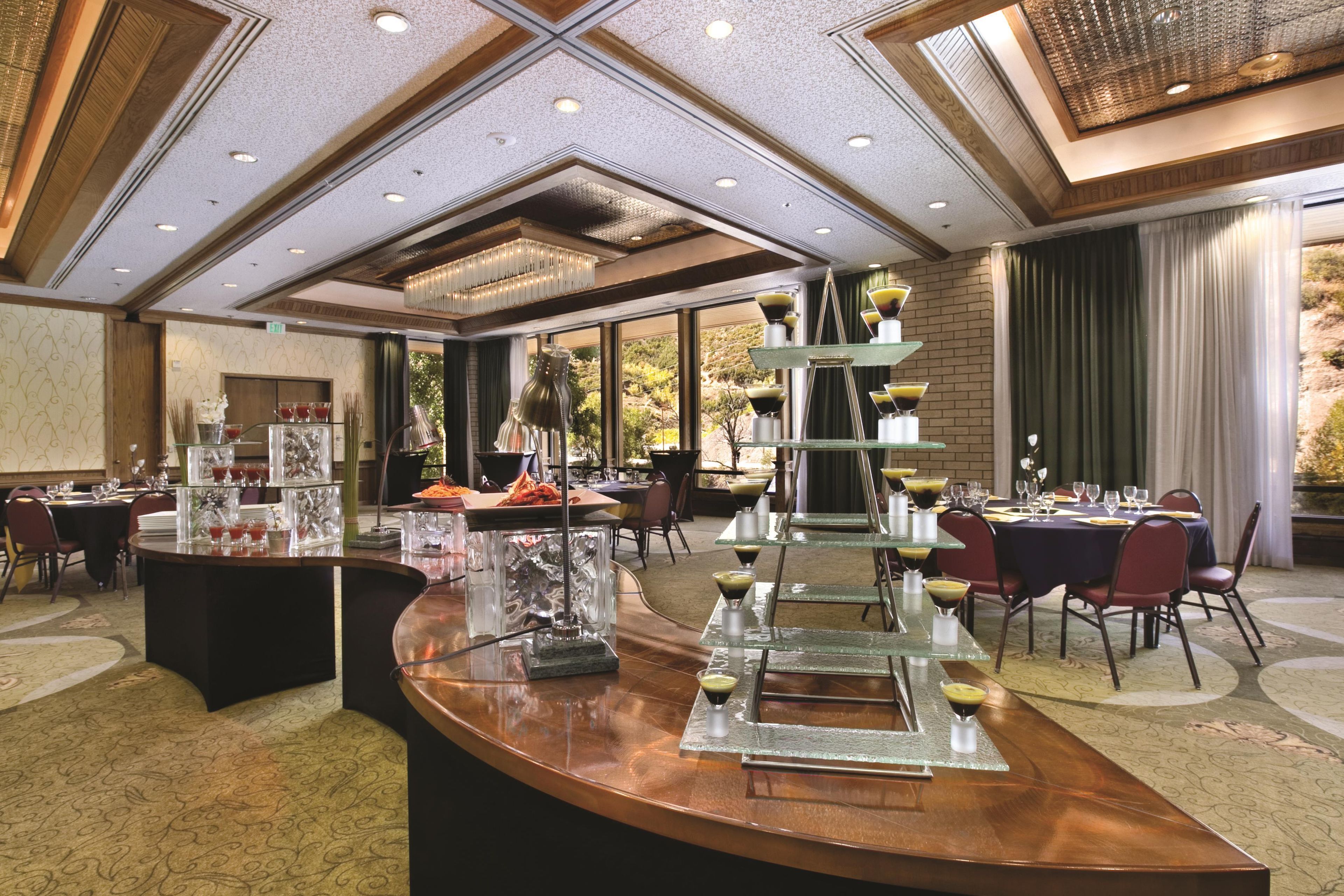 Un hall d’hôtel doté d’un comptoir d’accueil incurvé, d’un présentoir à boissons à plusieurs niveaux et offrant une vue sur l’extérieur grâce à de grandes fenêtres.