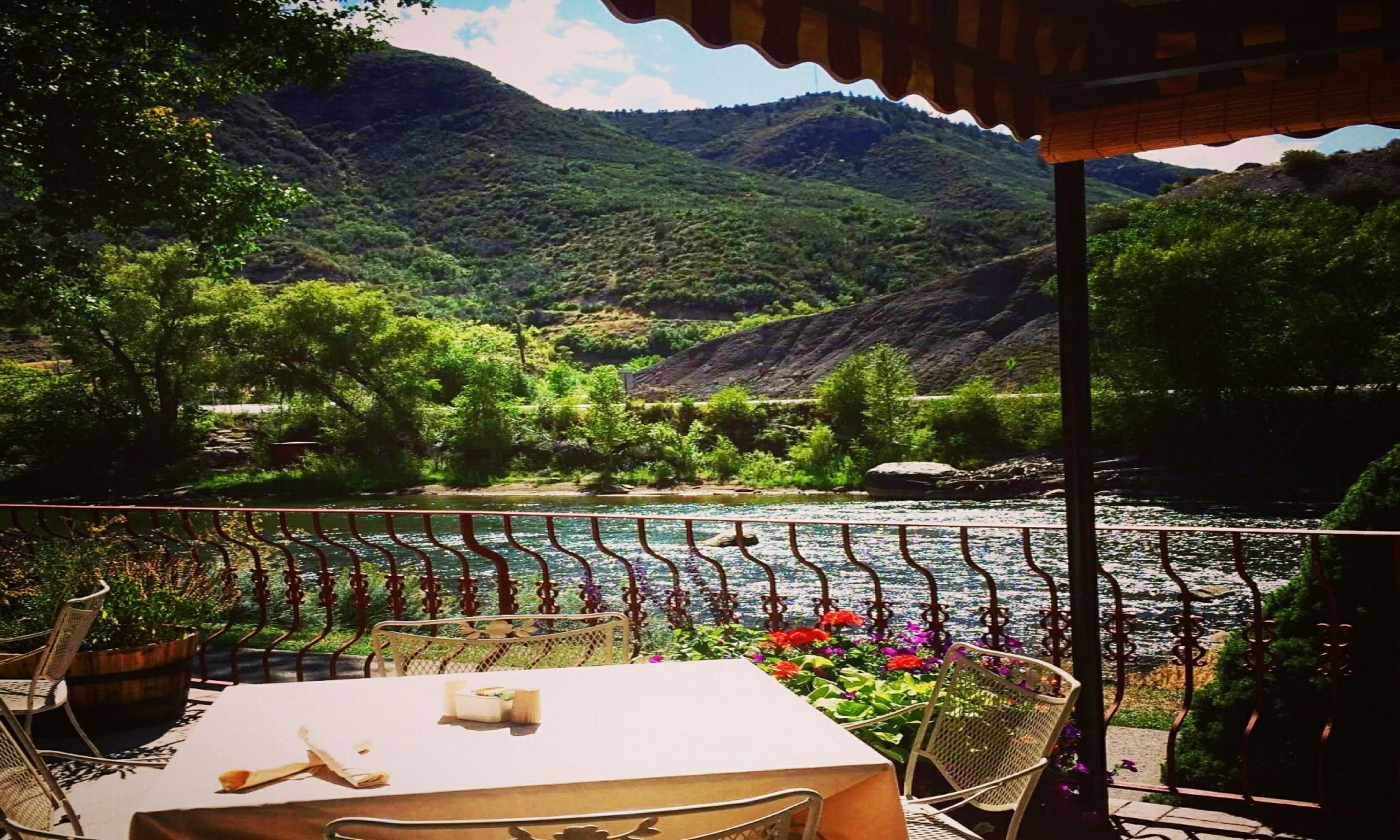 Eine Terrasse mit Tisch und Stühlen mit Blick auf einen Fluss und Berge.