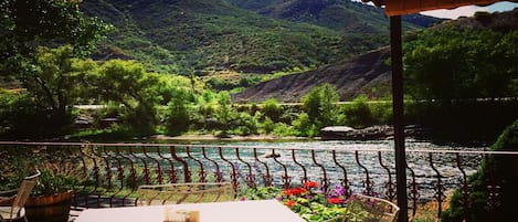 Eine Terrasse mit Tisch und Stühlen mit Blick auf einen Fluss und Berge.
