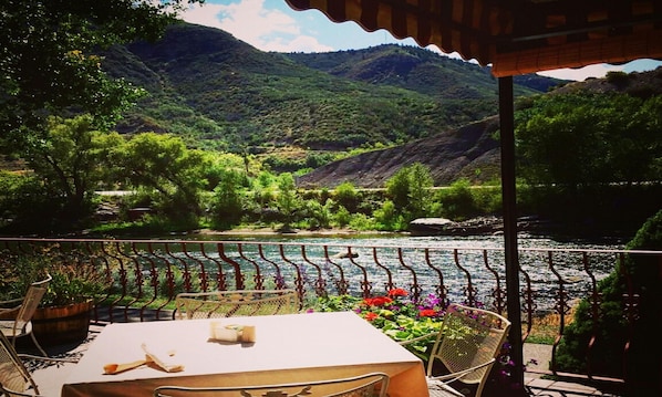 A terrace with a table and chairs overlooking a river and mountains.