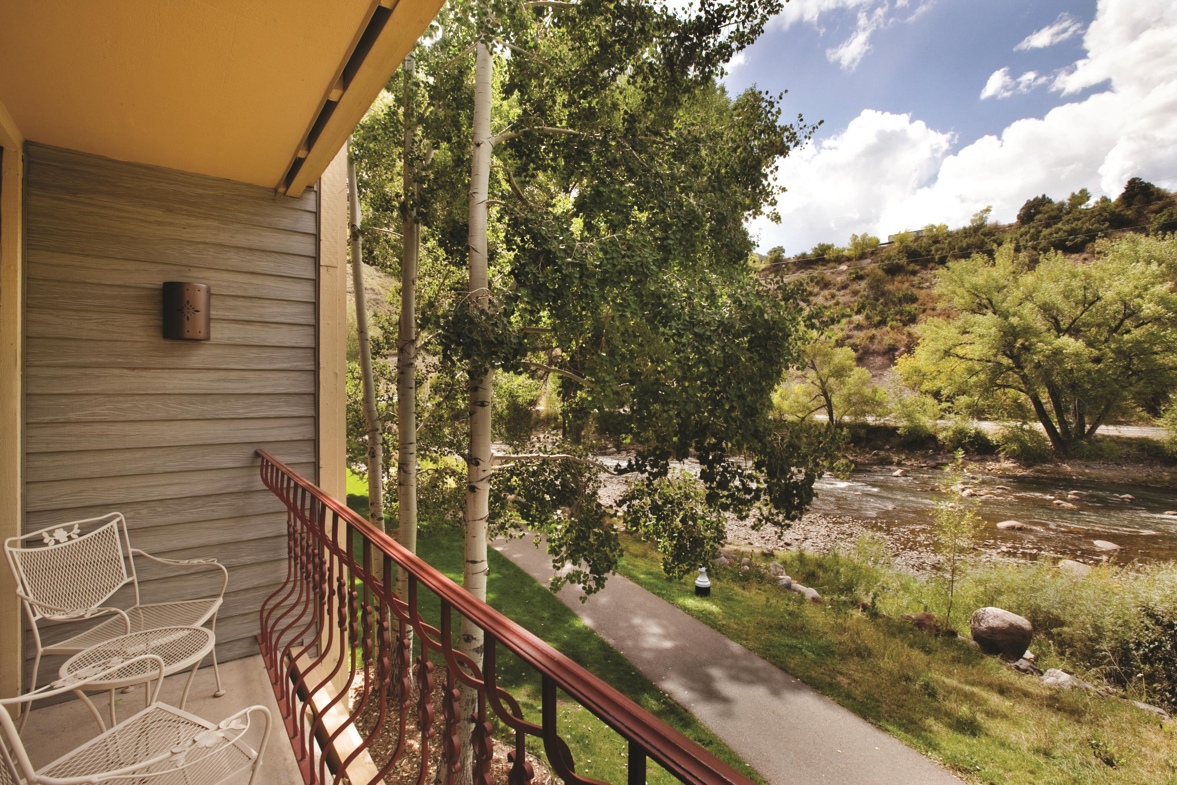 A wooden balcony with metal railings overlooking a garden with a pathway and trees.