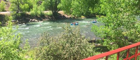 A river with people rafting, surrounded by lush greenery and a red railing.