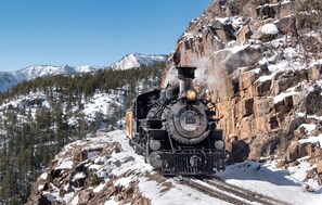 A steam locomotive on a snow-covered railway track with rocky terrain and snow-capped mountains in the background. - DoubleTree by Hilton Durango (Durango)