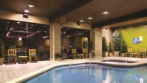 A swimming pool with chairs and tables, surrounded by brick walls and potted plants.
