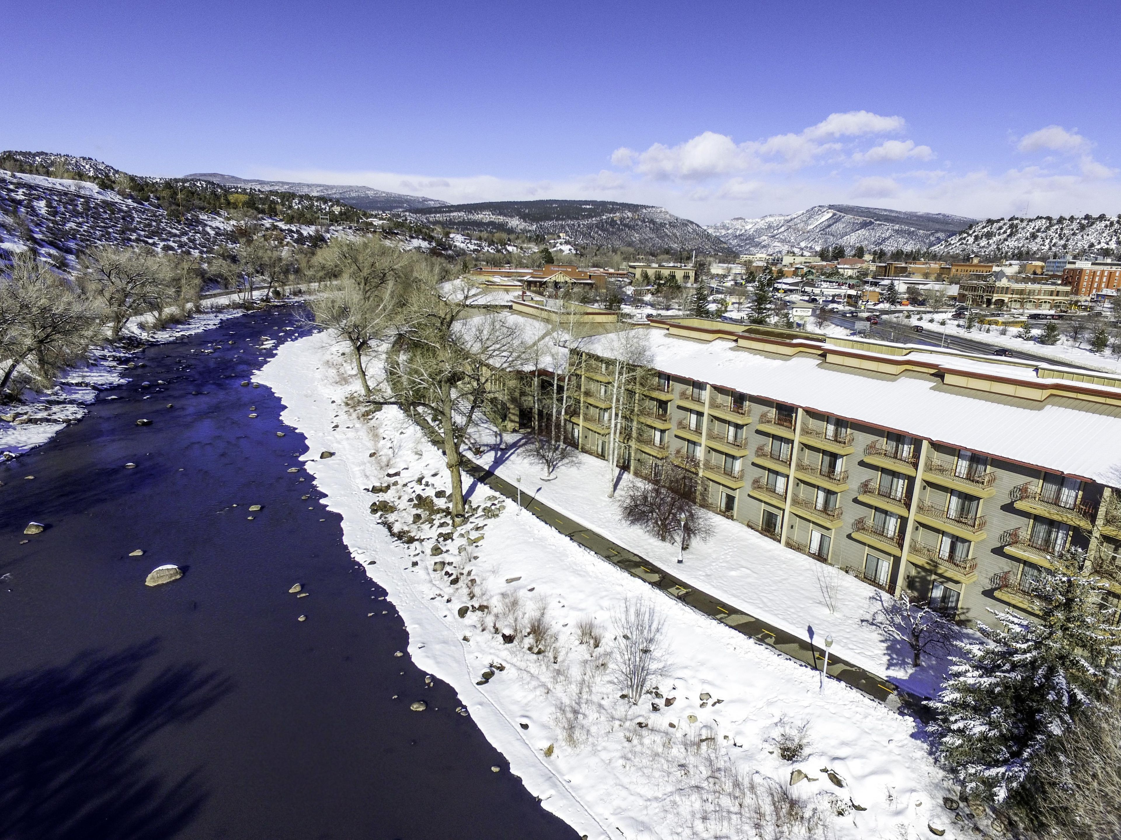 A hotel with a river running alongside, surrounded by snow-covered hills.