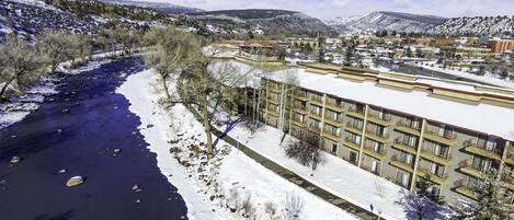A hotel with a river running alongside, surrounded by snow-covered hills.