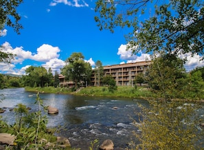 Un hotel con varios balcones con vistas a un río, rodeado de árboles y vegetación.