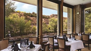 A restaurant with tables set for dining, large windows offering a view of a hillside.