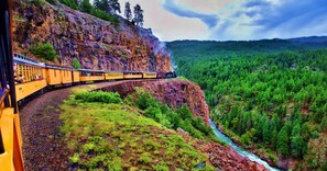 A train traveling along a track that winds through a mountainous area with a river and dense forest. - DoubleTree by Hilton Durango (Durango)