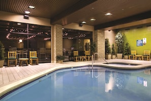 An indoor swimming pool with chairs and tables, a brick wall, and a caution sign.
