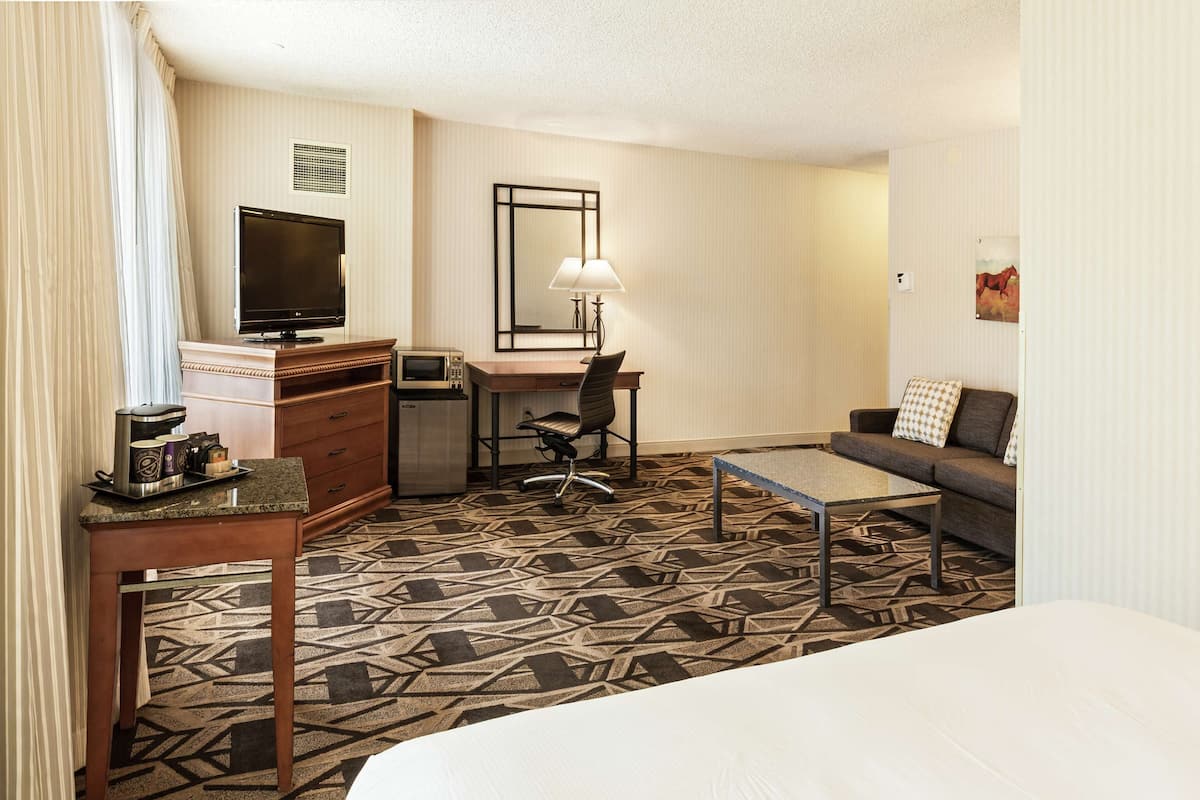 A hotel room with a bed, a desk with a computer, a television, a coffee maker, and a sofa.