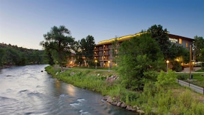 A riverside hotel with a well-maintained lawn, a clear view of the river, and a building with multiple balconies.