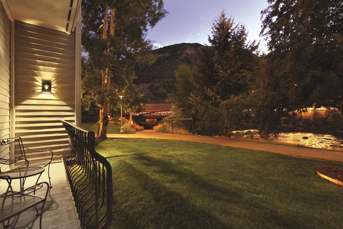 A well-maintained lawn with a patio area featuring metal chairs and a table, overlooking a body of water and a mountain backdrop.