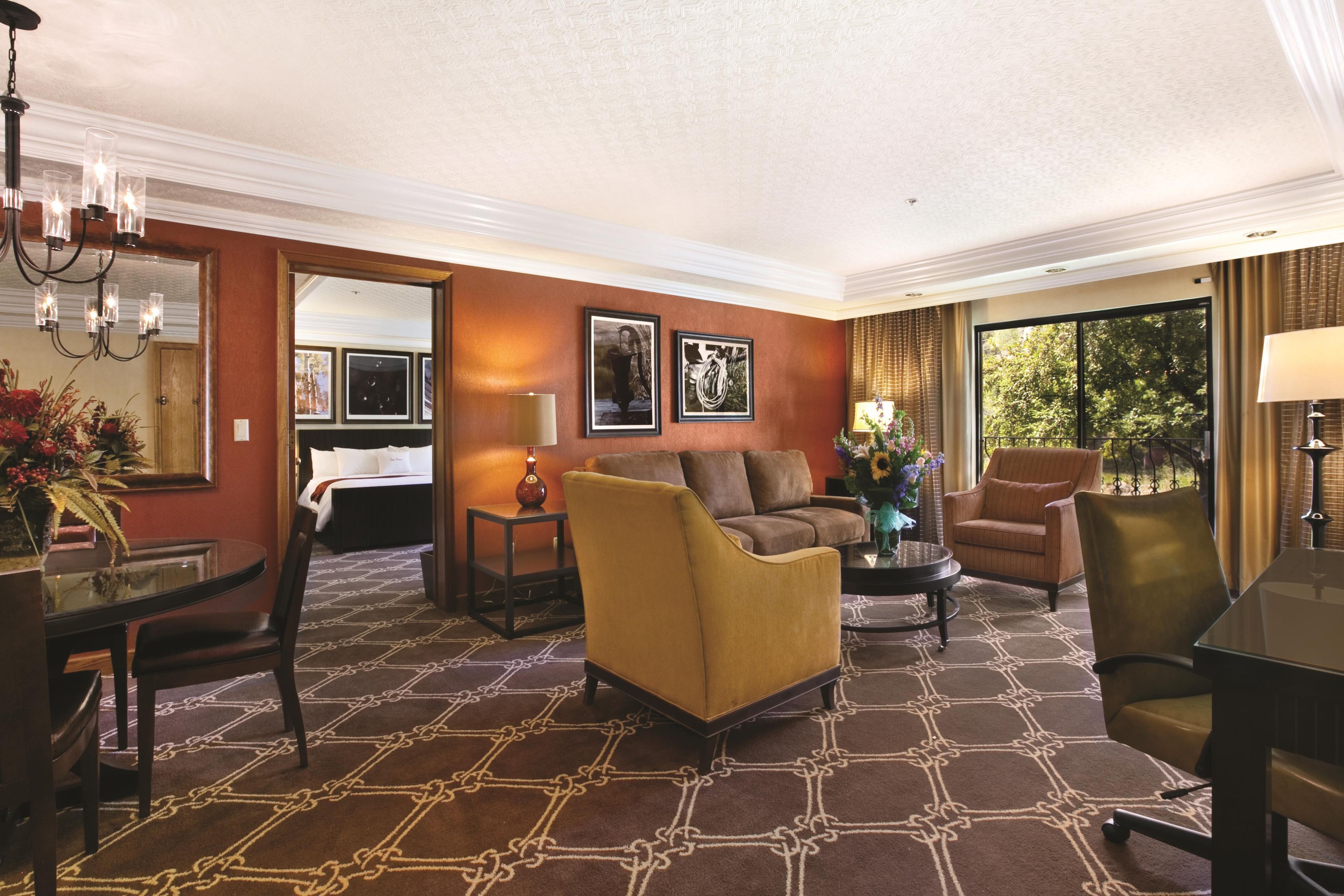 A hotel room with a patterned carpet, a sofa, a chair, a dining table, and a window with curtains.