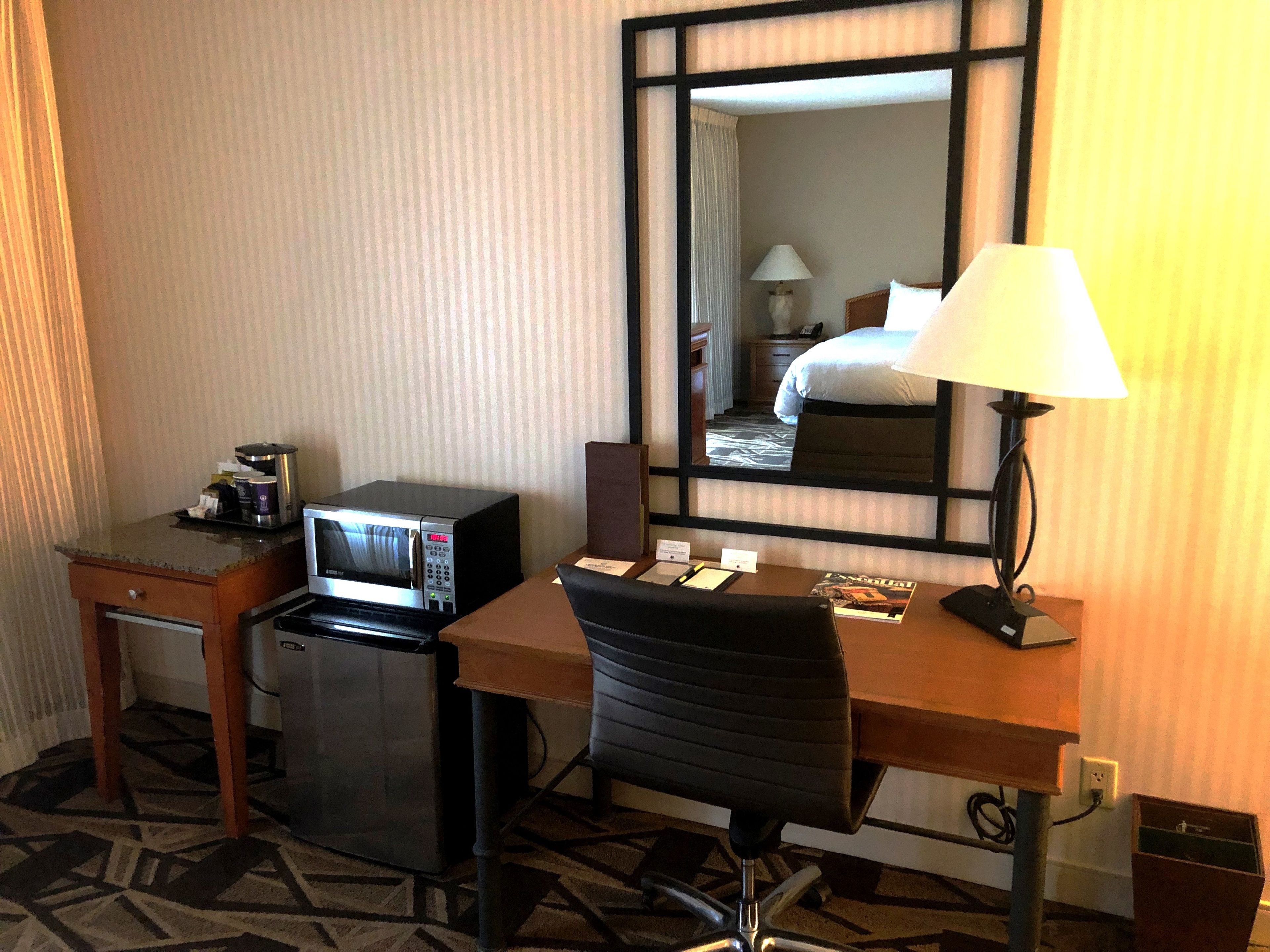 Hotelkamer met een bureau, magnetron, stoel, lamp en grote spiegel.