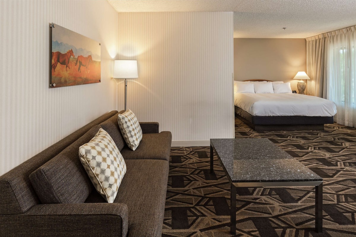 A hotel room with a sofa, a small table, a bed, and a painting on the wall.